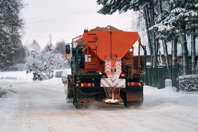 En snöplogsbil applicerar salt och sand medan lastbilen arbetar för att rengöra den snöiga vägen